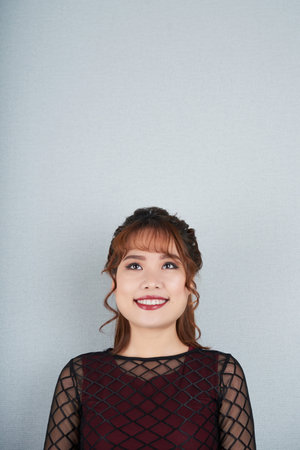 Beautiful smiling young woman looking up, isolated on grey