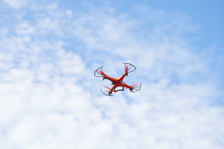 Orange drone with four rotos agianst blue sky