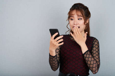 Shocked Vietnamese young woman reading message on smartphoneの写真素材