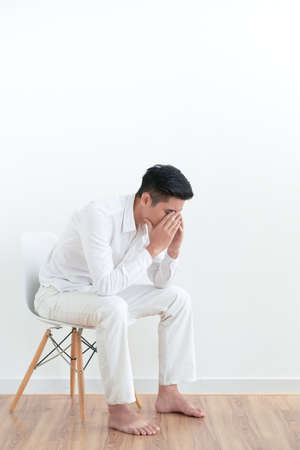 Tired frustrated young man sitting on chair and covering his face with armsの写真素材