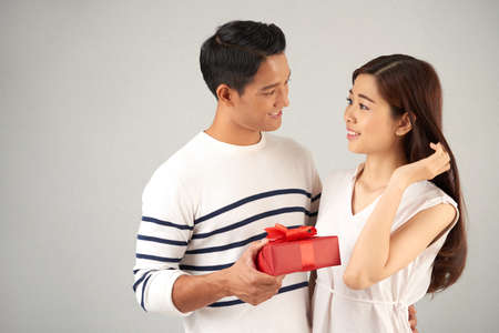 Celebrating Saint Valentines Day with Soulmate: handsome Asian man embracing his pretty young girlfriend while holding git box in hand, studio shotの写真素材