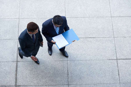 Business colleagues standing outdoors and discussing financial report, view from the topの写真素材