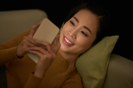 Smiling young woman checking text massages on her smartphone late at nightの写真素材