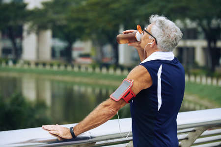 Senior sporty man standing on the bridge and drinking waterの写真素材