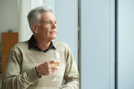 Pensive aged man looking through the window and drinking wineの写真素材