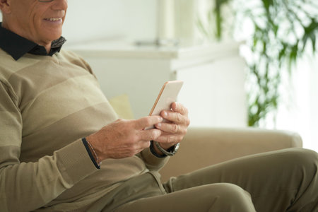 Cropped image of senior man sitting on the sofa with phone in his hands