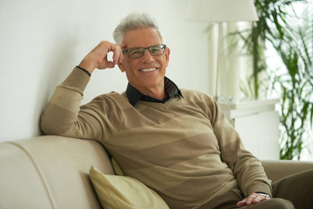Portrait of happy senior man sitting on sofa at homeの写真素材