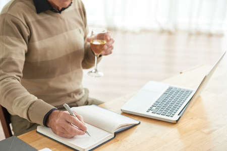 Man with glass of wine writing plans in his notepadの写真素材