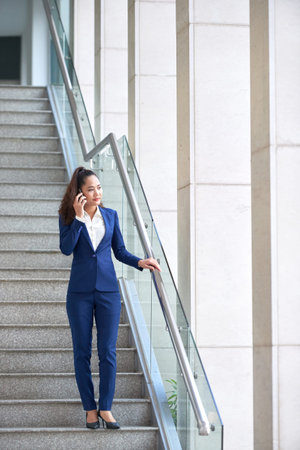 Young Asian businesss woman walking down the stairs and talking on the phoneの写真素材