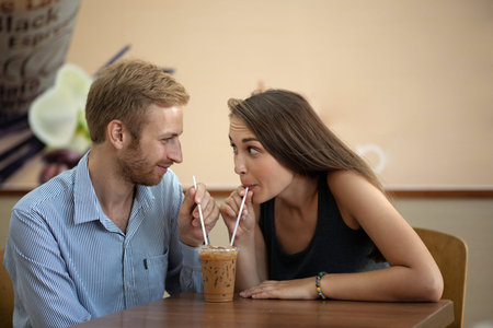 Young couple drinkink milkshake through straws from one plastic cupの写真素材
