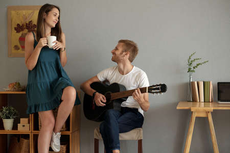 Happy young man playing guitar for his beautiful girlfriendの写真素材