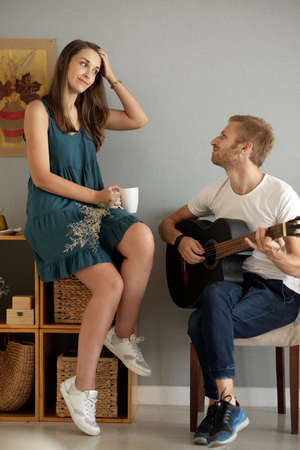 Young woman listening to her boyfriend playing acoustic guitar at homeの写真素材