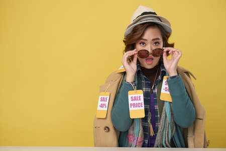 Portrait of surprised Asian woman wearing sunglasses and layers of clothes with sale labels, copy space to the leftの写真素材