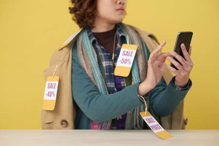 Young woman wearing clothes with sale labels using app on her smartphoneの写真素材
