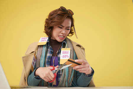 Portrait of angry Asian woman cutting her credit card with scissors to stop spending on shoppingの写真素材