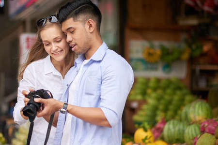 Mixed young couple of tourists reviewing photos on cameraの写真素材