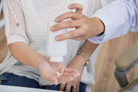 Close-up shot of unrecognizable doctor giving female patient pill while sitting at office desk, blurred backgroundの写真素材