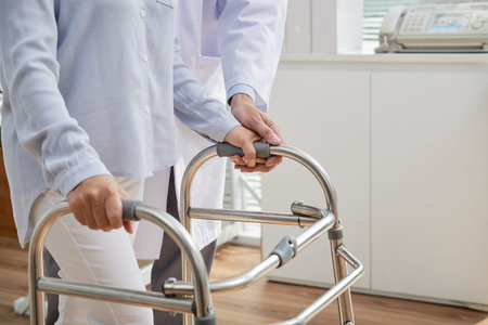 Unrecognizable physiotherapist wearing white coat standing next to female patient while helping her...