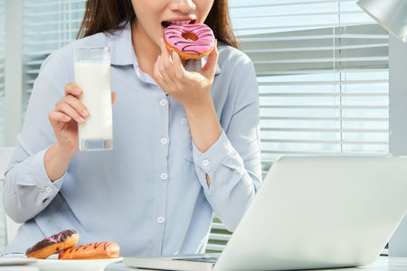 Business woman having doughnuts and glass of milk at her office table