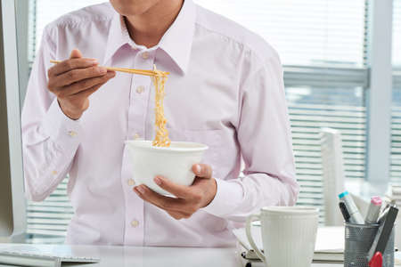 Cropped image of businessman eating instant noodles for lunchの写真素材