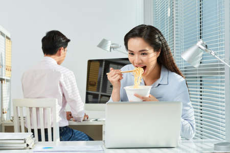 Pretty young business woman eating ramen when working in officeの写真素材