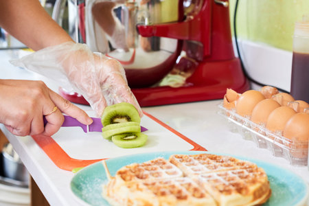 Hands of woman cutting kiwi to garnish wafflesの写真素材