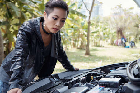Serious woman looking under the hood of her carの写真素材