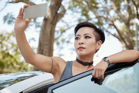 Pretty Vietnamese woman getting out of car and taking selfieの写真素材
