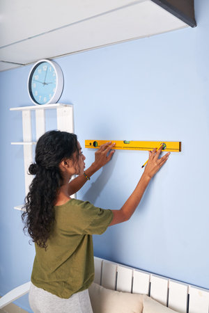 Young woman using construction level to measure the wall