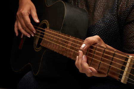 Close-up shot of unrecognizable musician wearing blouse and jeans playing acoustic guitar, black...