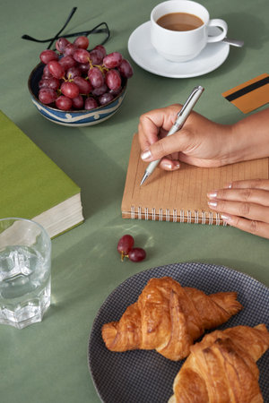 Close-up shot of businesswoman writing down ideas concerning promising project while having breakfast at kitchenの写真素材