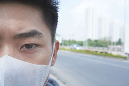 Face of Vietnamese young man in mask in polluted cityの写真素材