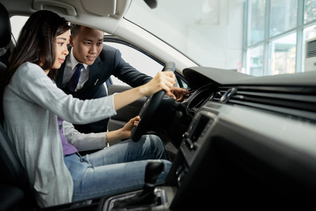 Young VIetnamese salesman showing dashboard and explaining automobile characteristics to female customerの写真素材
