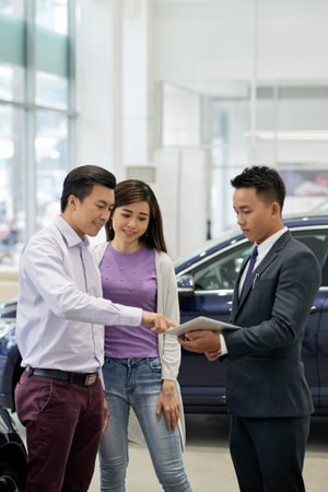 Vietnamese married couple choosing new car with help of assistant
