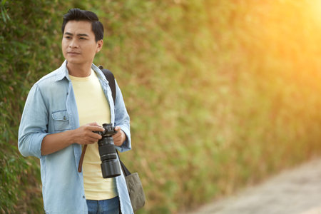 Portrait of pensive young Asian photographer standing in parkの写真素材