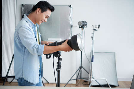 Cheerful Asian photographer setting light in photo studioの写真素材