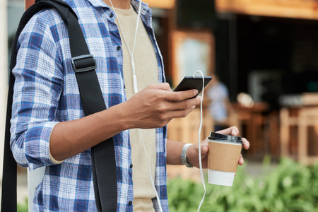 Close-up shot of unrecognizable man wearing T-shirt and checked shirt surfing Internet on smartphone...