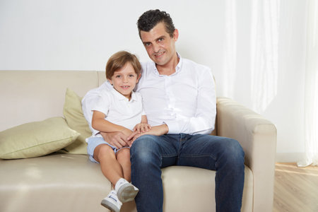 Cheerful man and his son sitting on sofaの写真素材