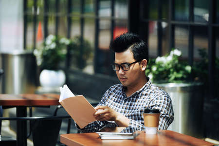 Vietnamese man having cup of coffee and reading his favorite bookの写真素材