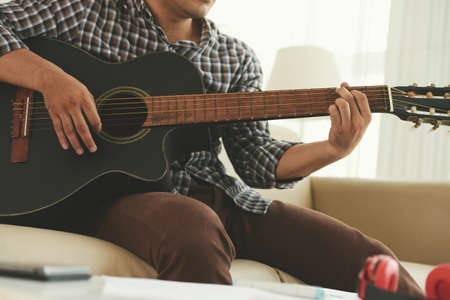 Cropped image of young man playing guitar at homeの写真素材