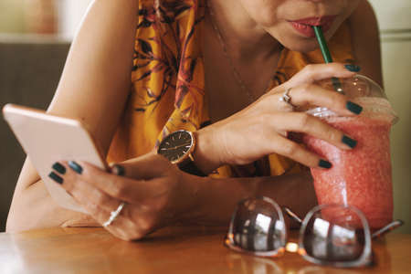 Close-up image of woman drinking cocktail and textingの写真素材