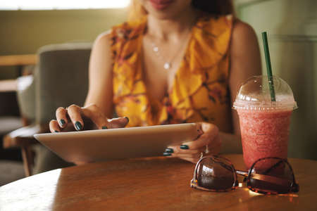 Close-up image of woman drinking smoothie in cafe and using application on digital tabletの写真素材