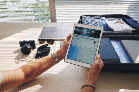Close-up of man holding touchpad and choosing a country for holidayの写真素材