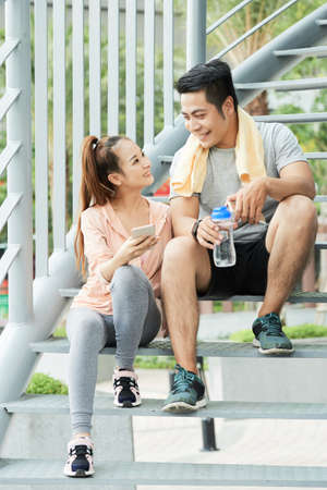Happy young VIetnamese couple resting on steps after trainingの写真素材