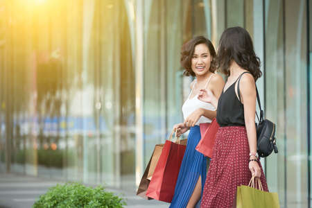 Young laughing Asian woman with shopping-bags leaving storeの写真素材