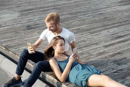Young couple resting outdoors and reading messages in smartphoneの写真素材