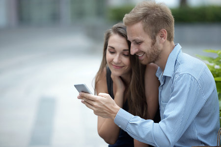 Cheerful pretty couple watching videos on smartphone screenの写真素材