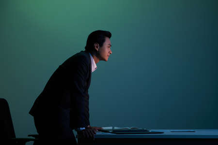 Asian businessman leaning on his table on dark backgroundの写真素材