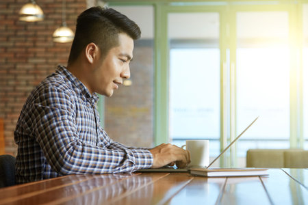 Asian man typing on his laptop while sitting at cafe