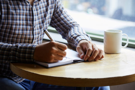 Close-up shot of unrecognizable manager taking notes while sitting at coffeehouse